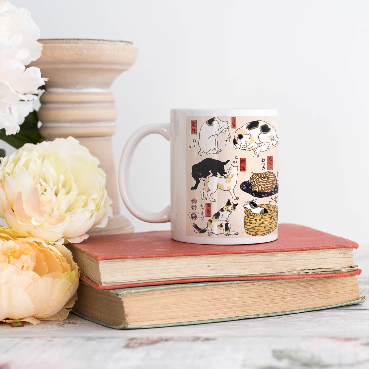 A ceramic mug printed with Utagawa Kuniyoshi's Japanese woodblock art "Tokaido Cats" standing on a pile of vintage books