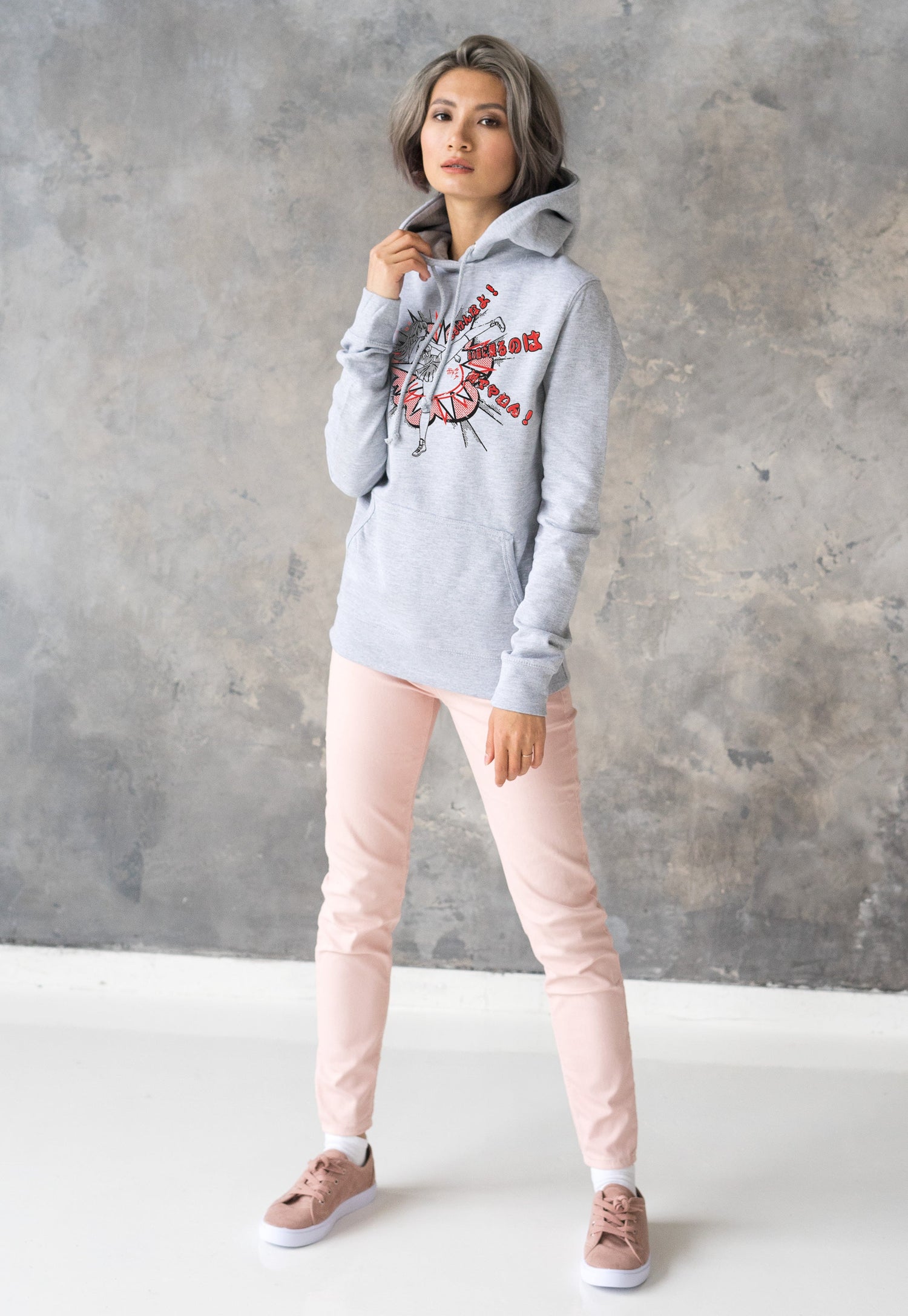 A young woman wearing a grey Hooded top with a print of a Japanese anime girl doing a high karate kick