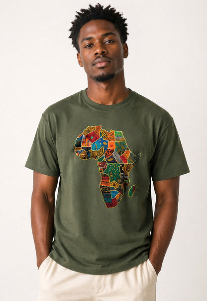 A man wearing an olive green t-shirt with a colorful, patterned graphic of the African continent on the chest, paired with light beige pants, against a plain off-white background.