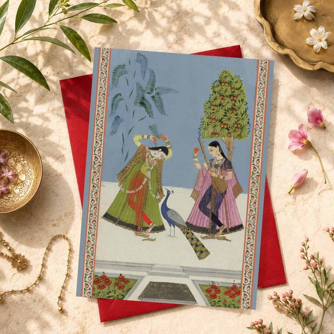 A large Indian art greeting card featuring Two Women and a Peacock (Gujara Ragini), ca. 1780.
Two elegantly dressed women stand beneath trees in this beautifully poised scene: one tunes a tanpura beneath a fruit-bearing mango tree, while the other reaches towards a branch and looks towards the peacock nearby.