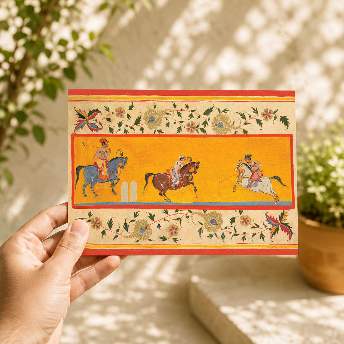 A large Indian art greeting card featuring Three Polo Players, early 17th century.
Three richly dressed riders sweep across a brilliant yellow field in this wonderfully lively miniature, their elegant horses caught mid-stride as the players lean into the game with mallets raised. 
